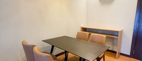 Una habitación con una mesa de comedor rectangular, cuatro sillas, un aire acondicionado de pared y una lámpara en el techo.