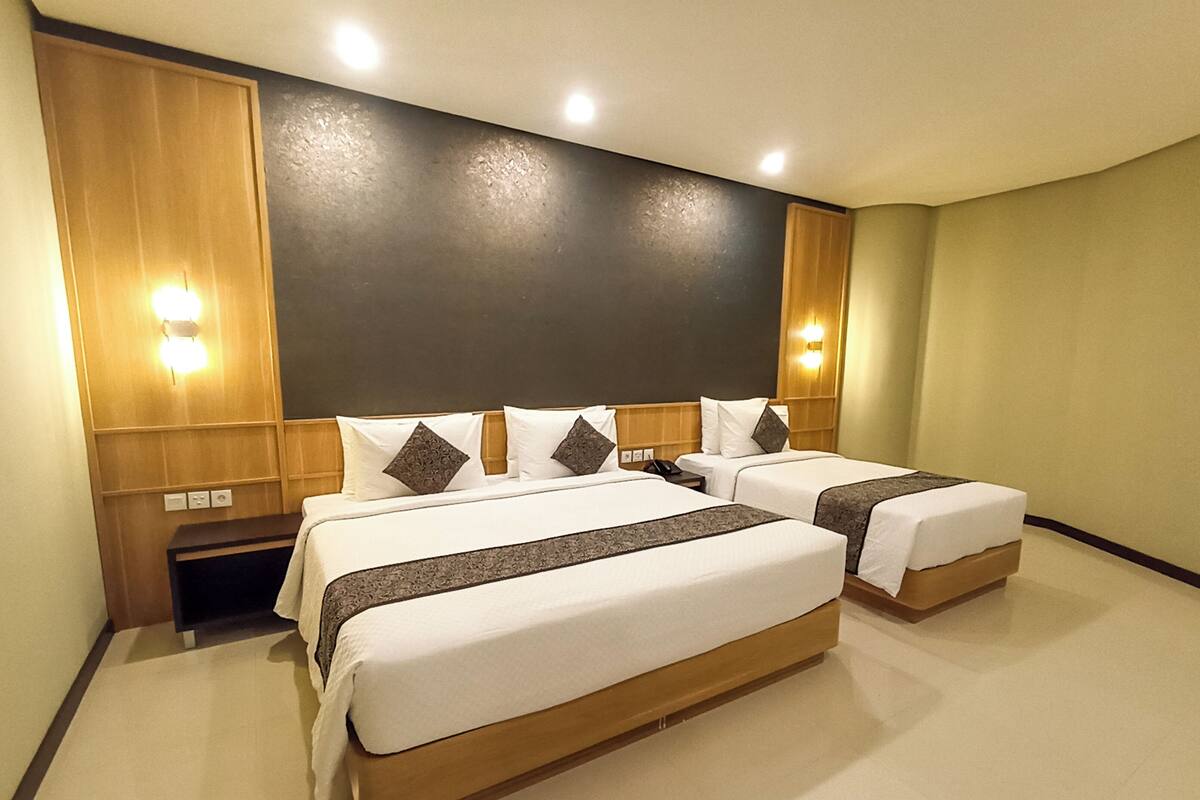 A hotel room with two beds, a wooden headboard, a nightstand, and wall-mounted lighting.