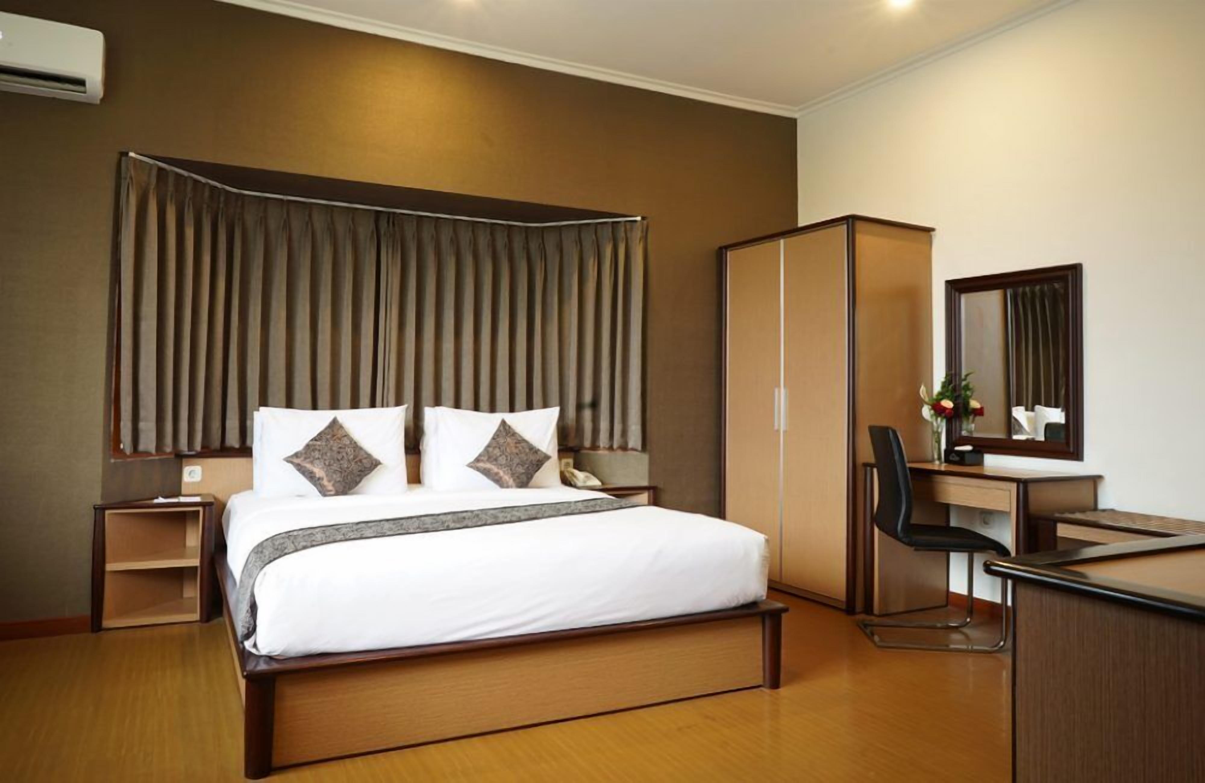 A hotel room with a large bed, a desk, a chair, a wardrobe, and a mirror.