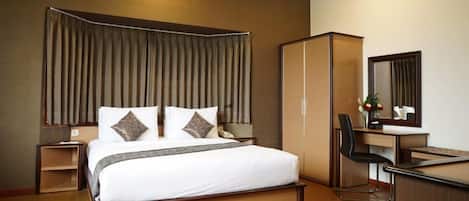Habitación de hotel con una cama grande, un escritorio, una silla, un armario y un espejo.