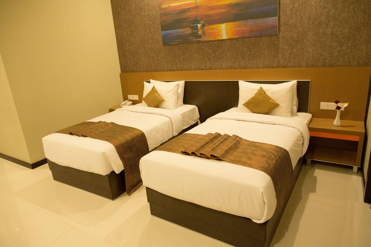 A hotel room with two beds, each with white linens and brown accents, a nightstand with a phone, and a painting above the beds.