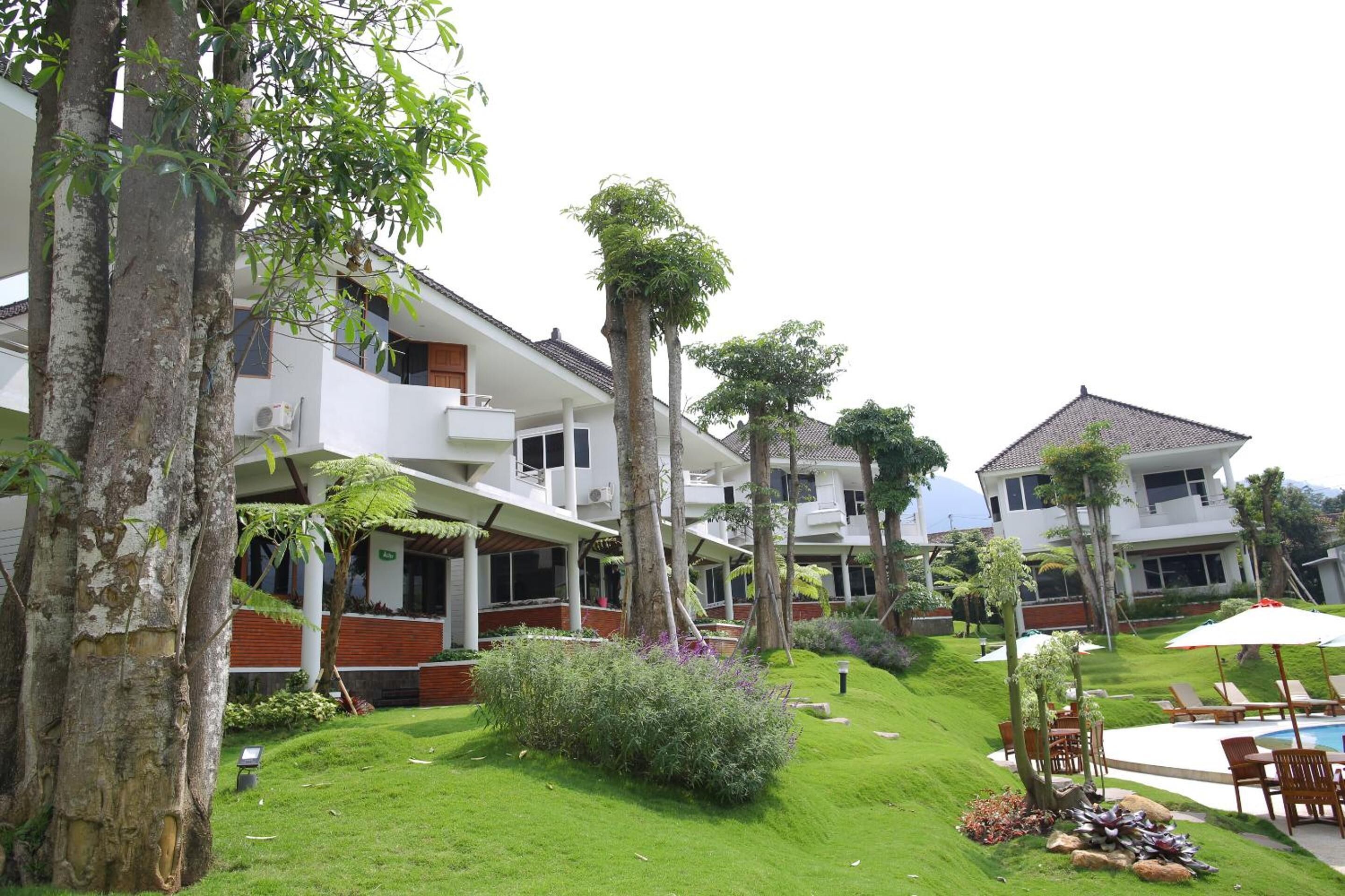A hotel with multiple buildings, a well-maintained lawn, and a swimming pool area.