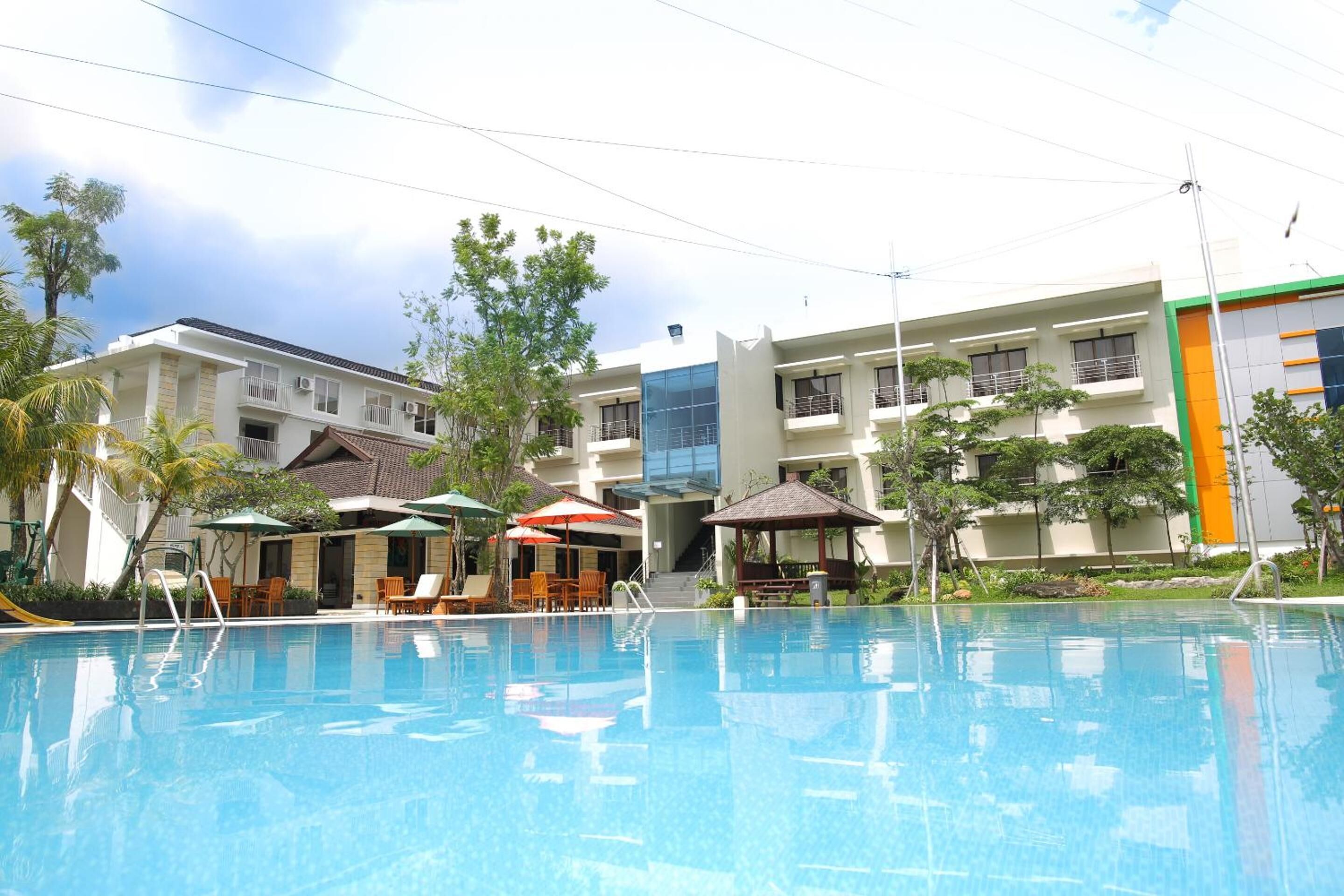 A swimming pool with lounge chairs and umbrellas, surrounded by multi-story buildings with balconies and outdoor seating areas.