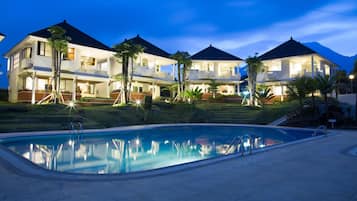 A hotel with a swimming pool, multiple balconies, and a well-lit exterior at dusk.