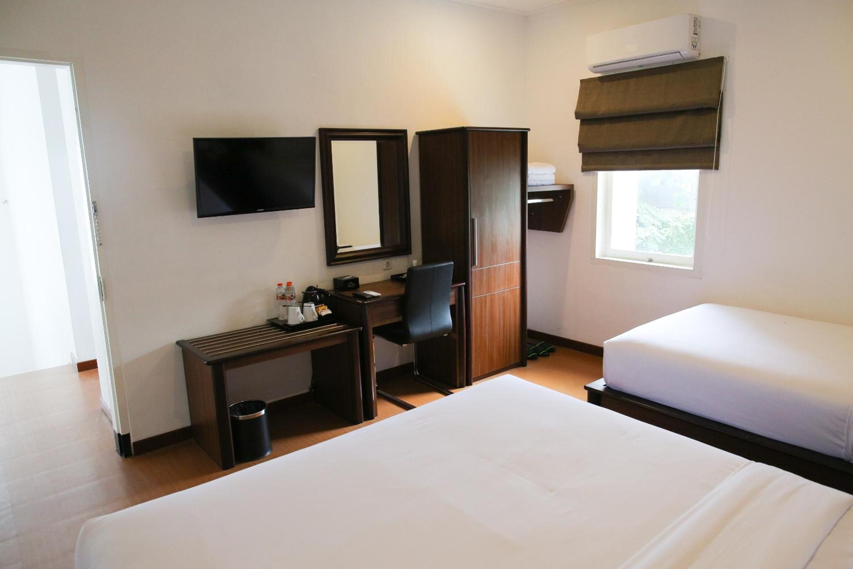 Habitación de hotel con cama, escritorio y silla, televisor, armario y ventana con persianas.