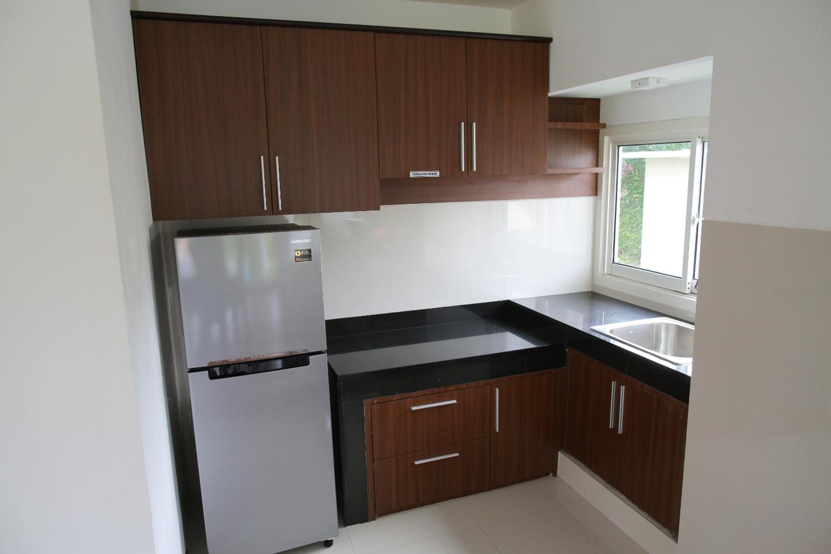 A kitchen with dark wooden cabinets, a stainless steel refrigerator, and a black countertop.