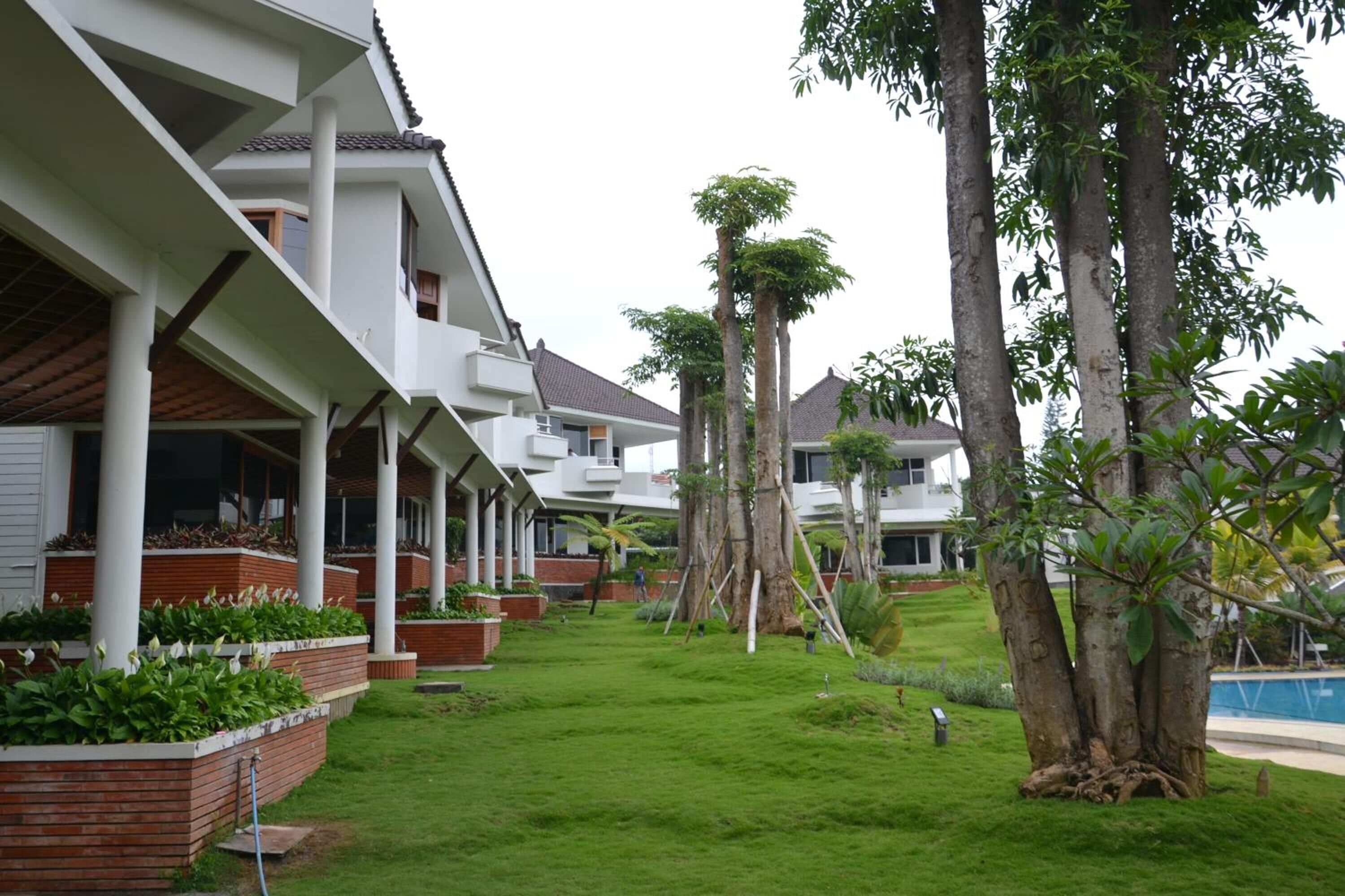 A modern hotel with a covered outdoor area, a swimming pool, and lush greenery.