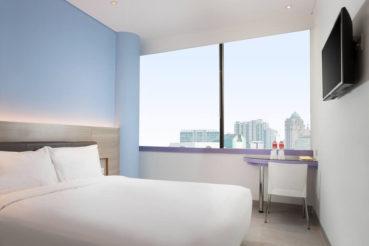 Habitación de hotel moderna con cama, escritorio y ventana grande con vista a la ciudad.