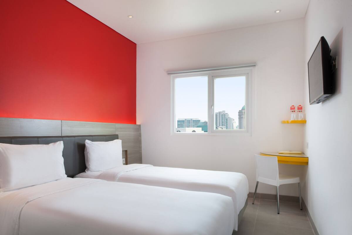 Habitación de hotel con dos camas, un escritorio, un televisor y una ventana con vista a la ciudad.
