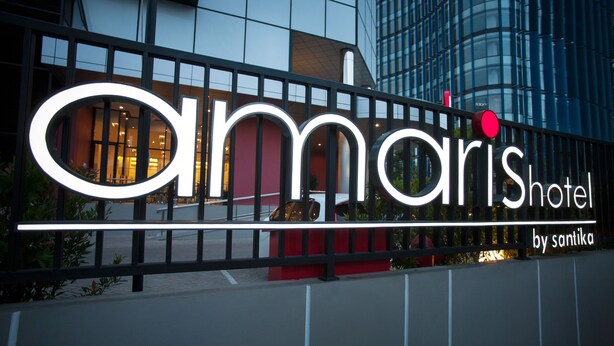 Un cartell d'hotel amb el nom 'Amaris Hotel by Santika' i un edifici modern al fons.