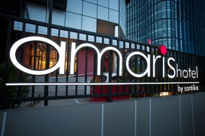 Un cartel de hotel con el nombre "Amaris Hotel by Santika" y un edificio moderno al fondo.
