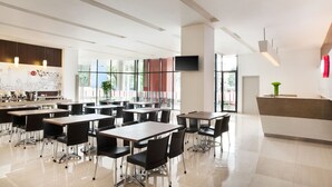 Una zona de dinar moderna amb taules i cadires, una recepció i un gran finestral amb vista a l'exterior.