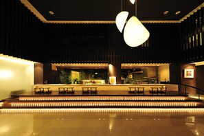 Un vestíbulo moderno con zona de bar, asientos escalonados e iluminación ambiental.