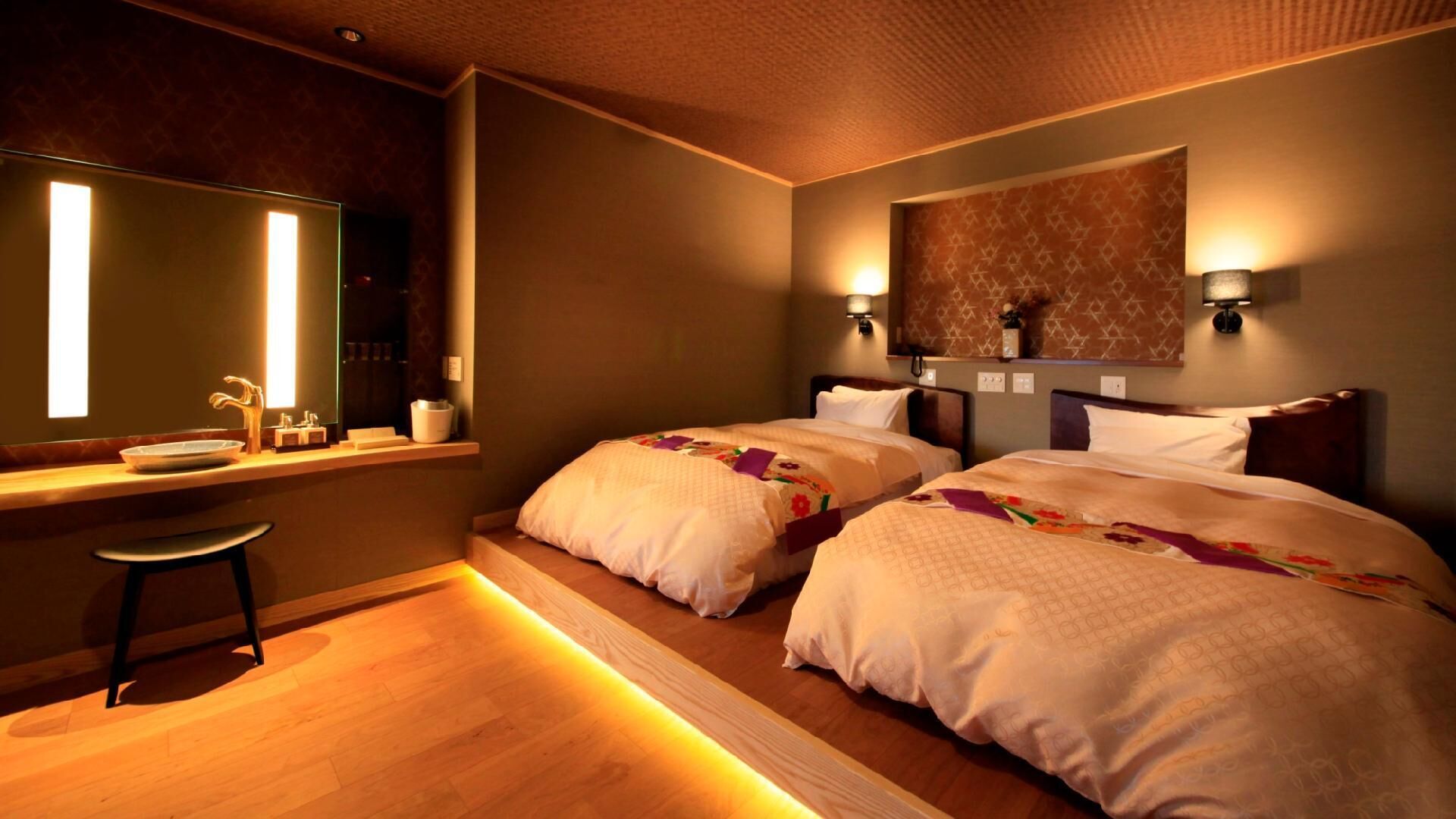A hotel room with two beds, a large mirror, a desk with a sink, and a wooden floor.