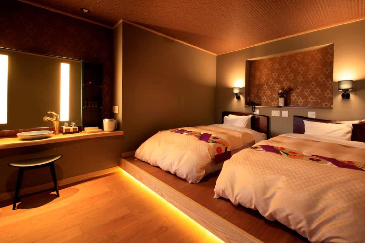 Une chambre d’hôtel avec deux lits, un grand miroir, un bureau avec un lavabo et un plancher en bois.