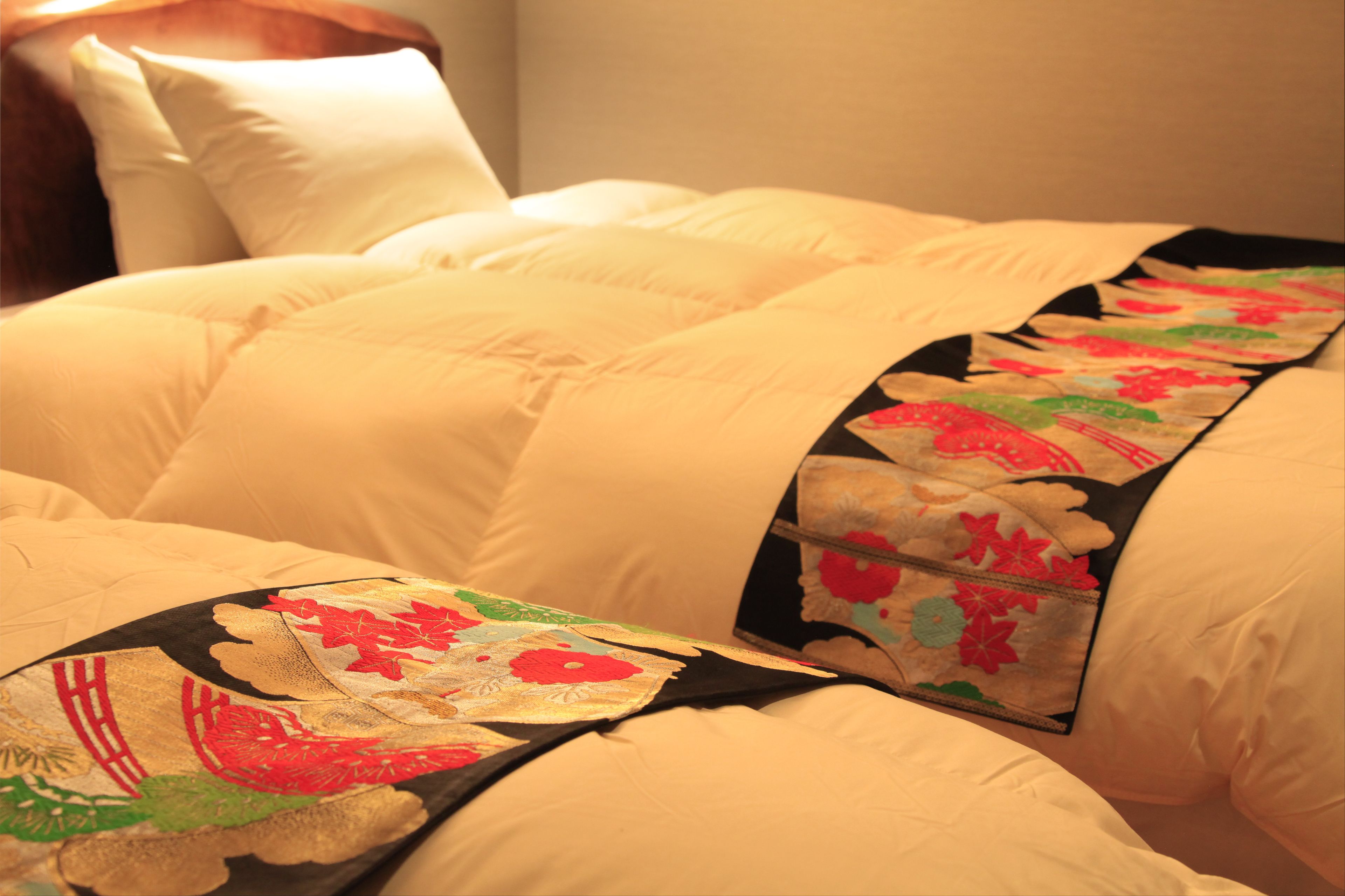 A bed with a quilted white duvet and a decorative pillow with floral patterns.