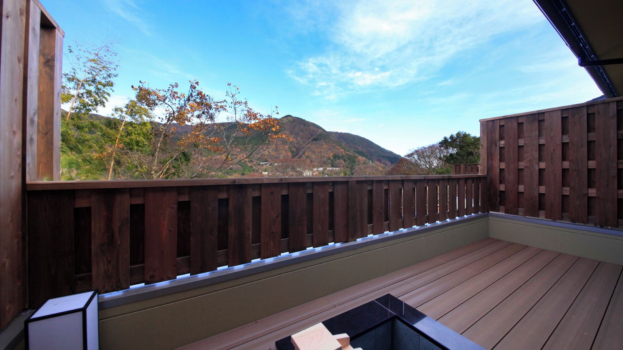 Una terraza de madera con vistas a una cadena montañosa y follaje otoñal.