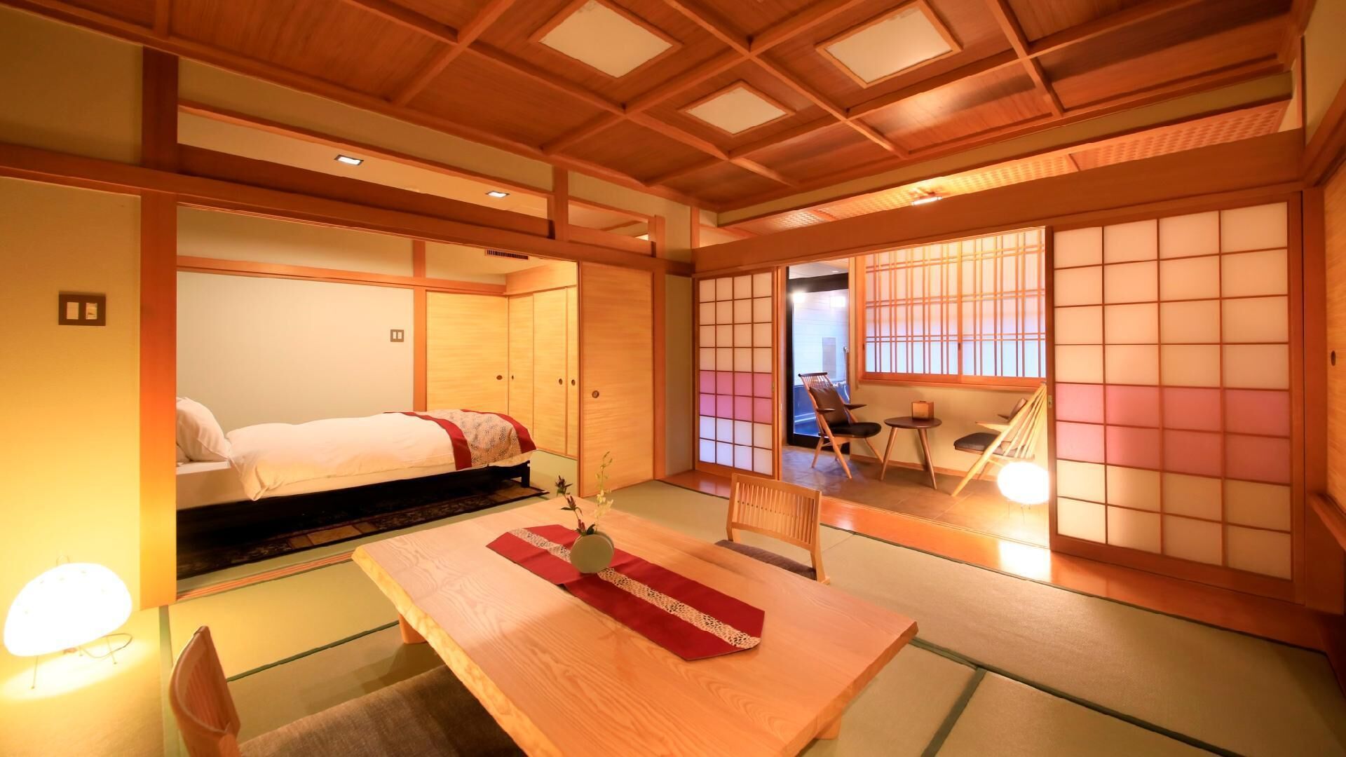 A traditional Japanese-style room with tatami flooring, a low wooden table, a bed with a futon, sliding doors, and a view through a shoji screen.