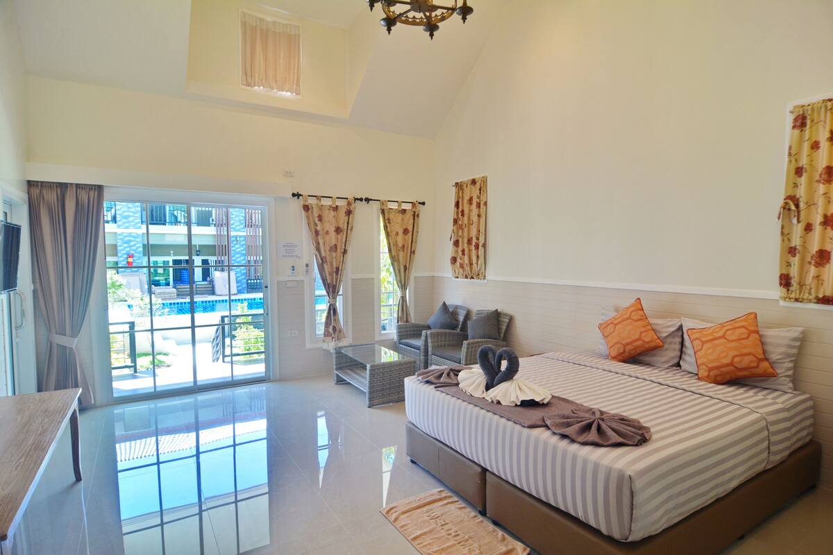 A spacious bedroom with a large bed, a sofa, and a glass door leading to a balcony.