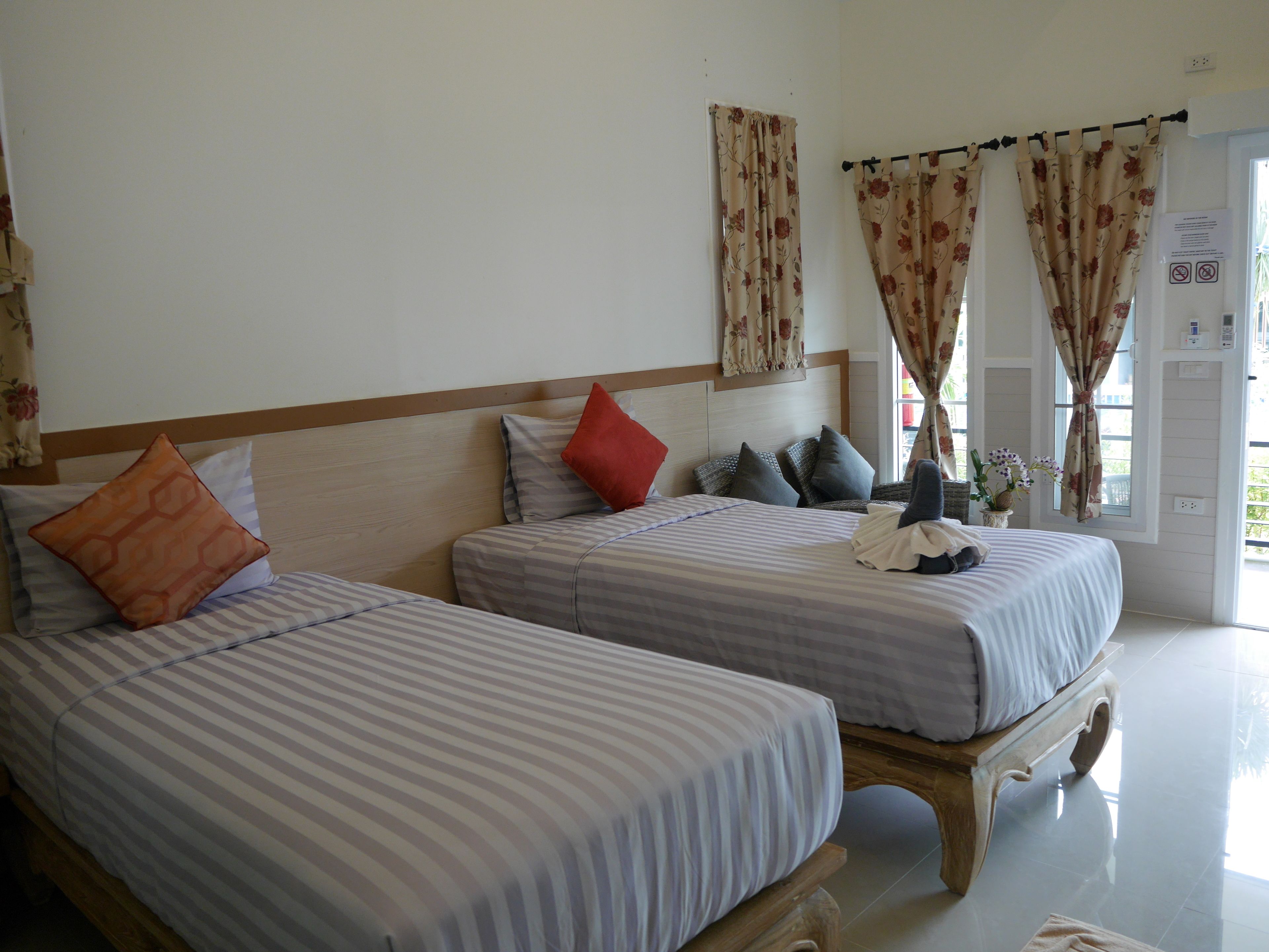 Habitació d'hotel amb dos llits, cadascun amb roba de llit i almoades a vares, un capçal de fusta i una finestra amb cortines.