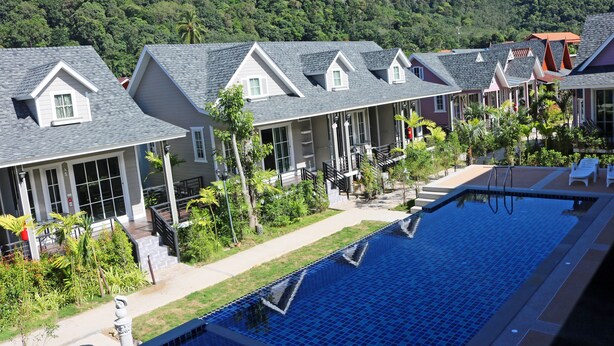 Un hotel con varias unidades, techos a dos aguas, piscina y abundante vegetación.