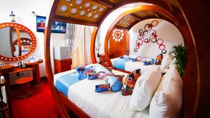 A bedroom with a circular arch design, a bed with multiple pillows, a bedside table, a mirror, and a television on the wall. - Hotel White House (Anuradhapura)