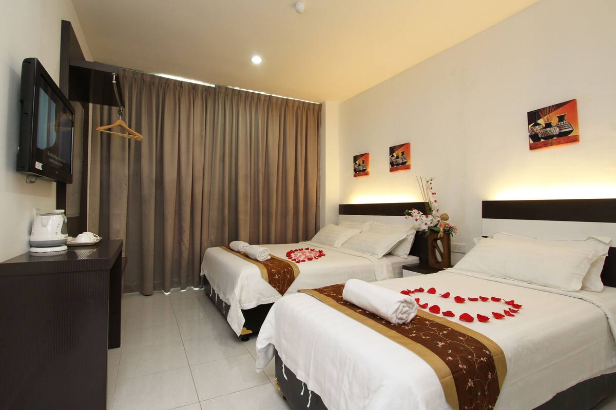 Quarto de hotel com duas camas, televisão, escrivaninha e cortina.