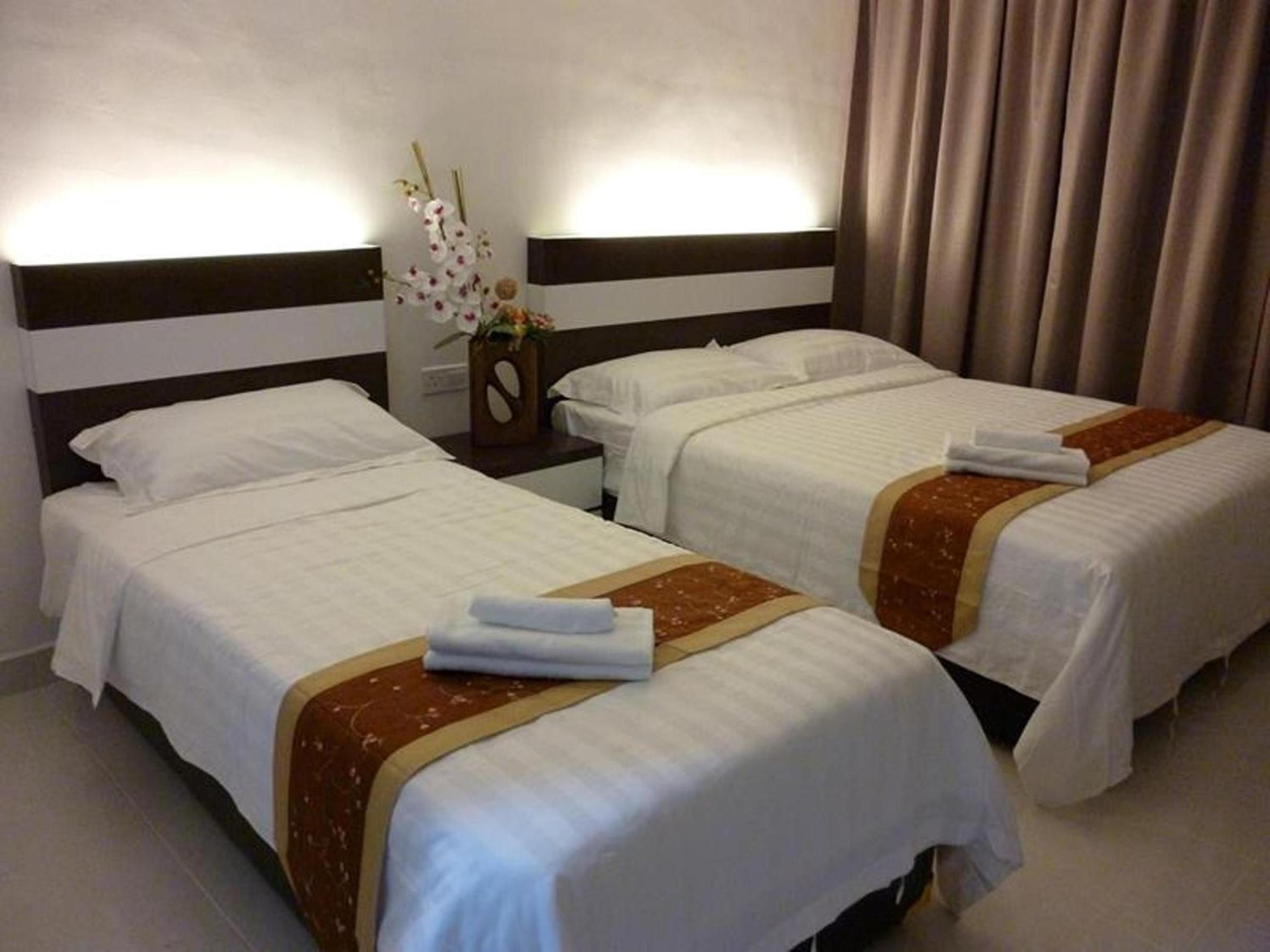 A hotel room with two beds, each with white bedding and a brown accent. There is a nightstand with a vase of flowers between the beds.