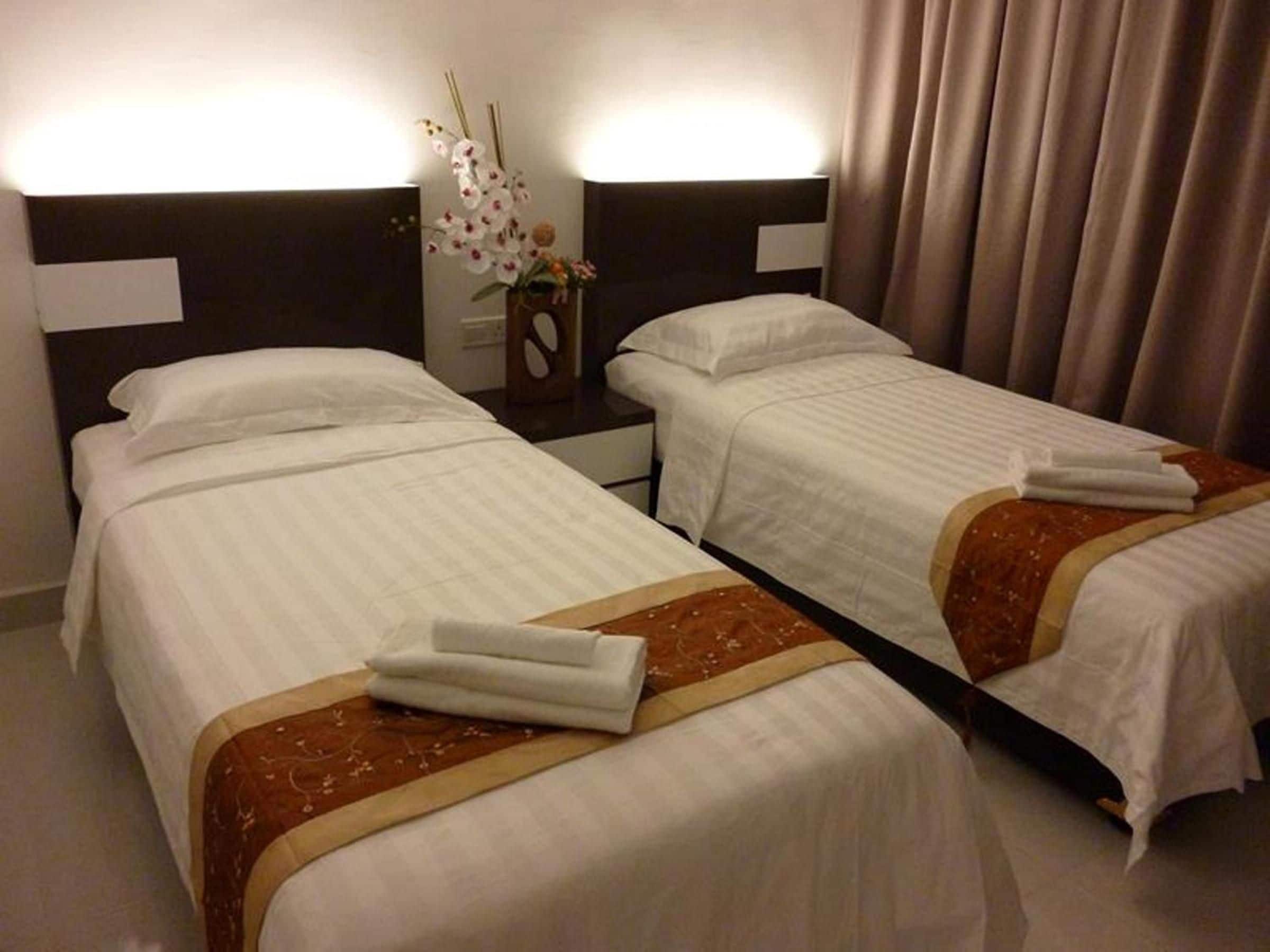 A hotel room with two beds, each with white linens and a brown decorative border. There is a nightstand with a vase of flowers between the beds.