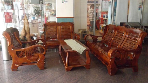 Un espacio de descanso con muebles de madera, incluyendo sofás y una mesa, en una habitación con puertas de cristal que dan a otro espacio.