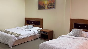 Quarto de hotel com duas camas, uma mesa de cabeceira com rádio, um quadro na parede e uma luminária no teto.