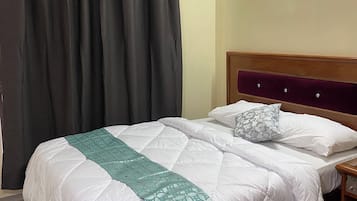 A hotel room with a large bed, a wooden headboard, a nightstand, and a window with curtains.