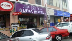 Un hotel con un letrero morado, coches estacionados y una fachada visible.