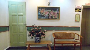 Zona de recepción con una puerta verde, un banco, una planta en maceta, un banco de madera y un letrero en la pared.