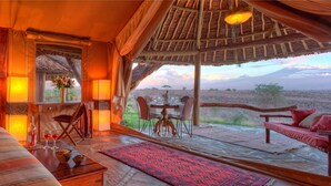 A room with a bed, a dining table with chairs, and a view of the landscape. - Elewana Tortilis Camp (Amboseli)