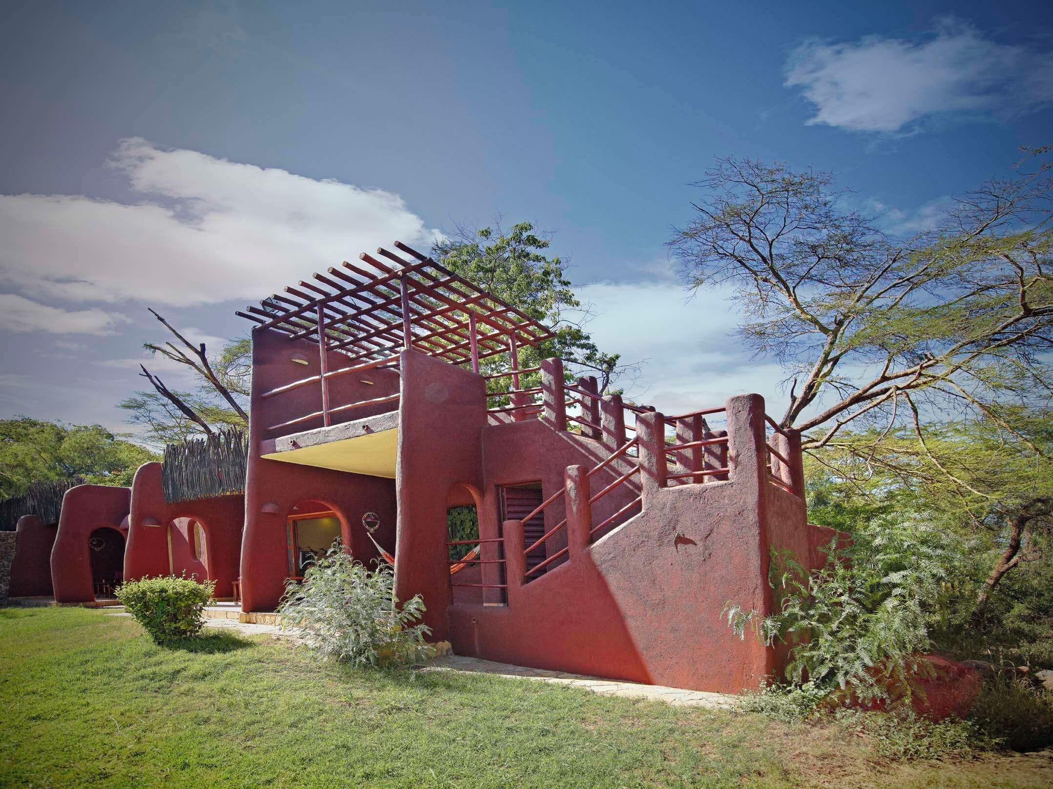 A red building with a unique architectural design, featuring a pergola-like structure on the roof and a staircase leading to an upper level.
