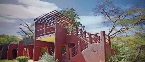 A red building with a unique architectural design, featuring a pergola-like structure on the roof and a staircase leading to an upper level.