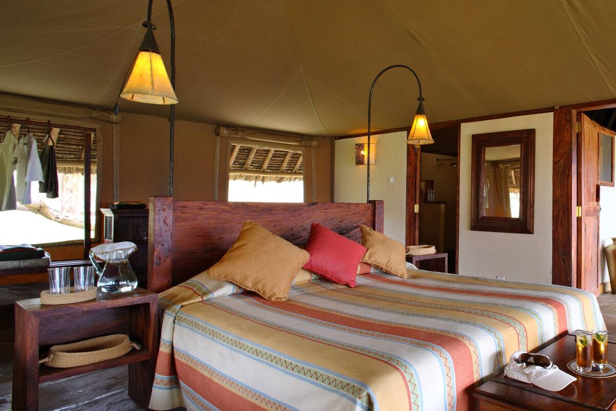 Une pièce spacieuse avec un grand lit, un bureau en bois et une chaise. Il y a une fenêtre donnant sur l’extérieur, et une lampe suspendue au plafond.