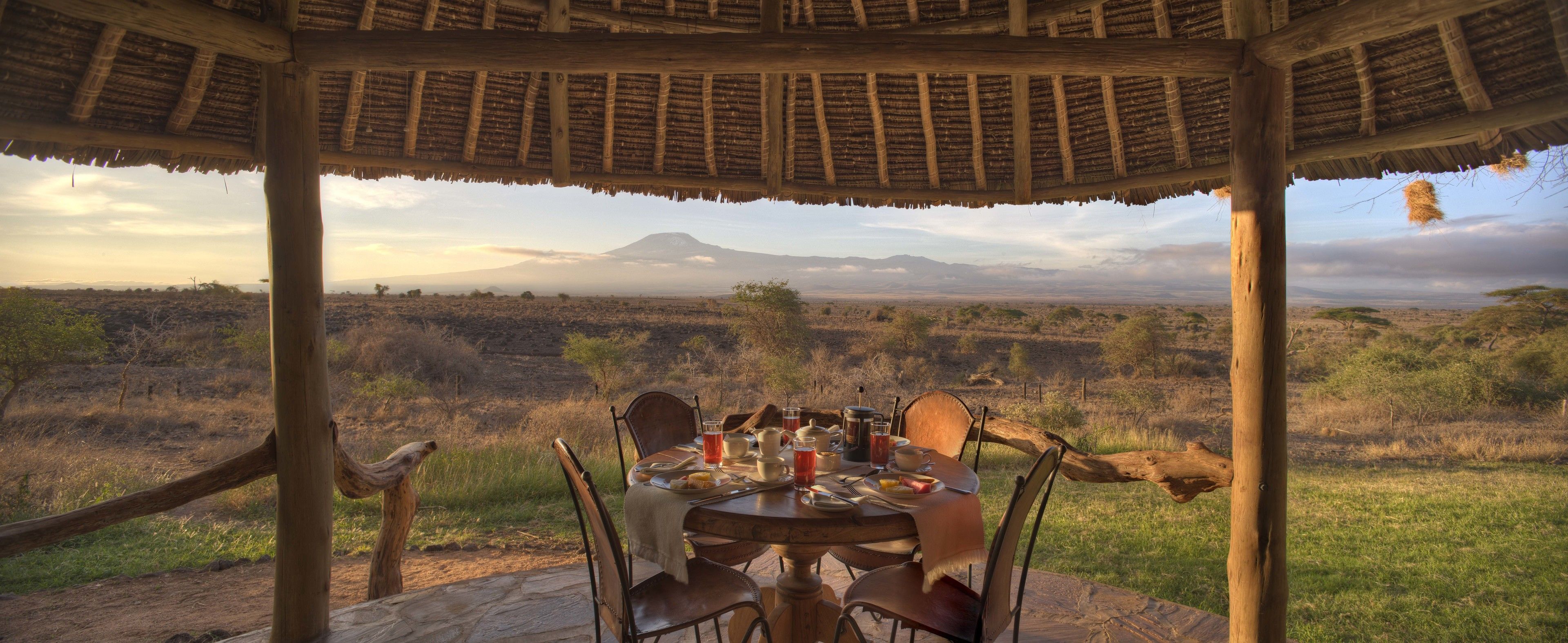 Un coin repas avec une table dressée pour quatre personnes, donnant sur un paysage de savane avec une montagne à l’horizon.