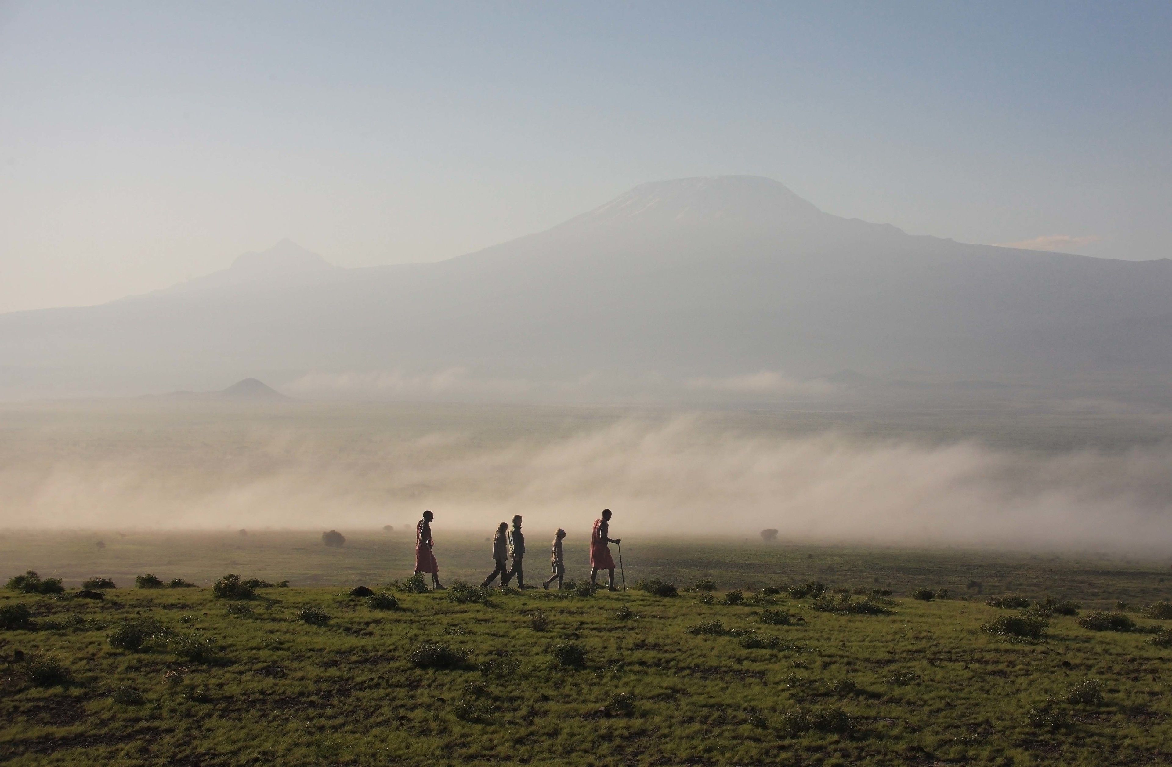 Paisaje llano con una montaña al fondo y un grupo de personas caminando.