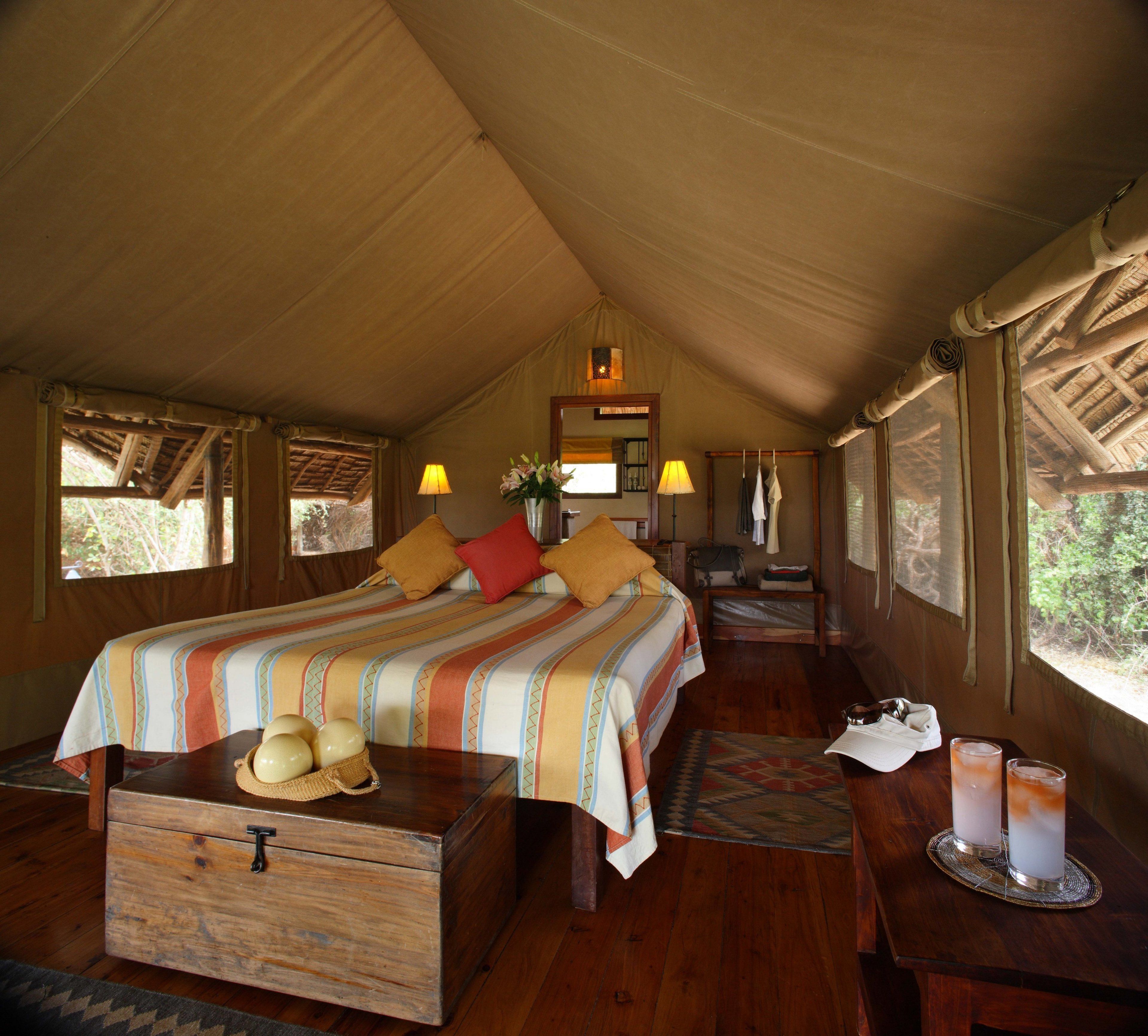 A spacious tented room with a large bed, wooden furniture, and a view of the outdoors.