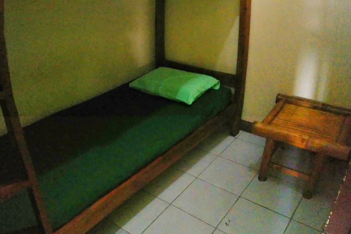 A bunk bed with a green mattress and a small wooden stool beside it.