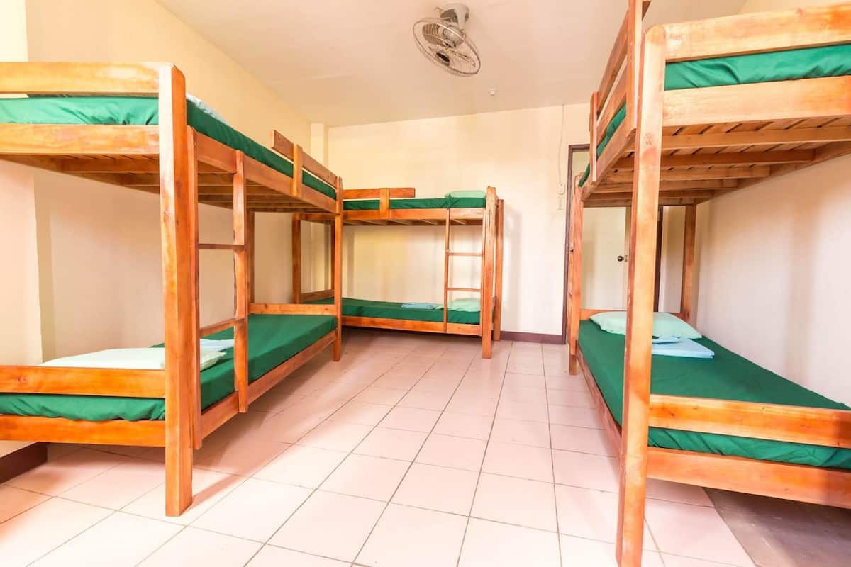 A dormitory room with four bunk beds, a ceiling fan, and tiled flooring.