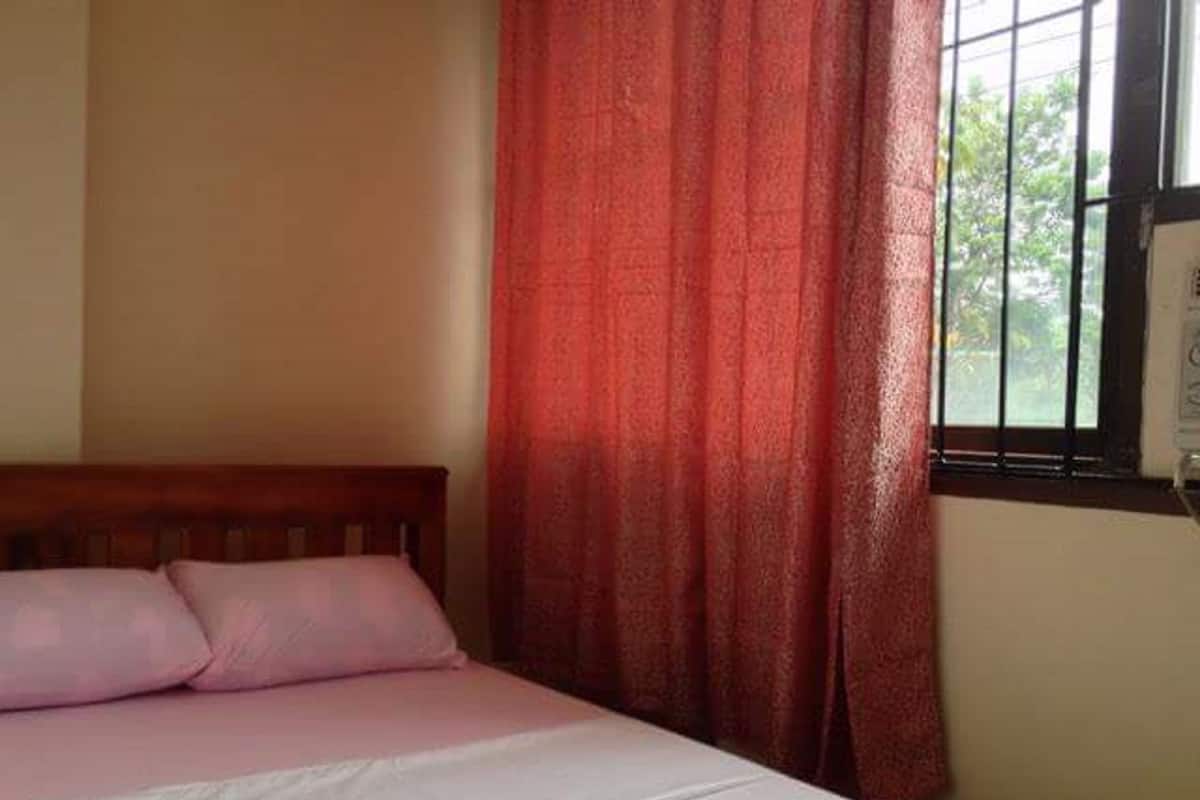 A single bed with a wooden headboard, a pink bedspread, and a red patterned curtain partially drawn to the side.