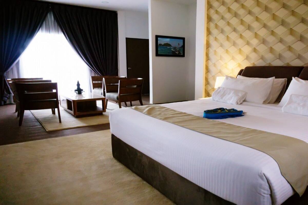 A hotel room with a large bed, a desk with chairs, and a view of the sea through the window.