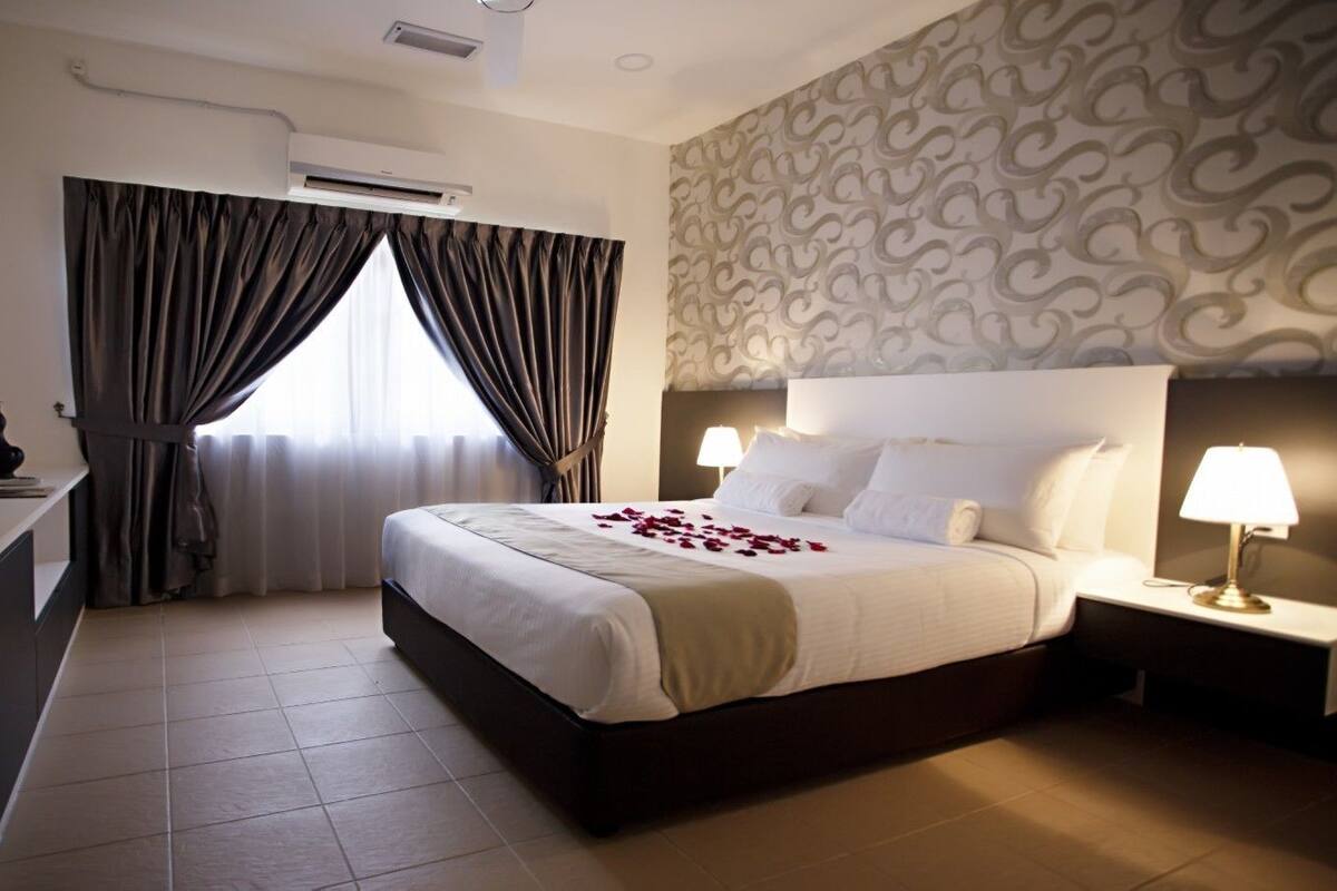 A hotel room with a bed, bedside tables, a desk, and an air conditioning unit.