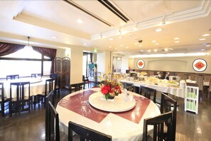 A restaurant with round tables, a buffet area, and a decorative centerpiece. - Chofu Urban Hotel (Chofu)