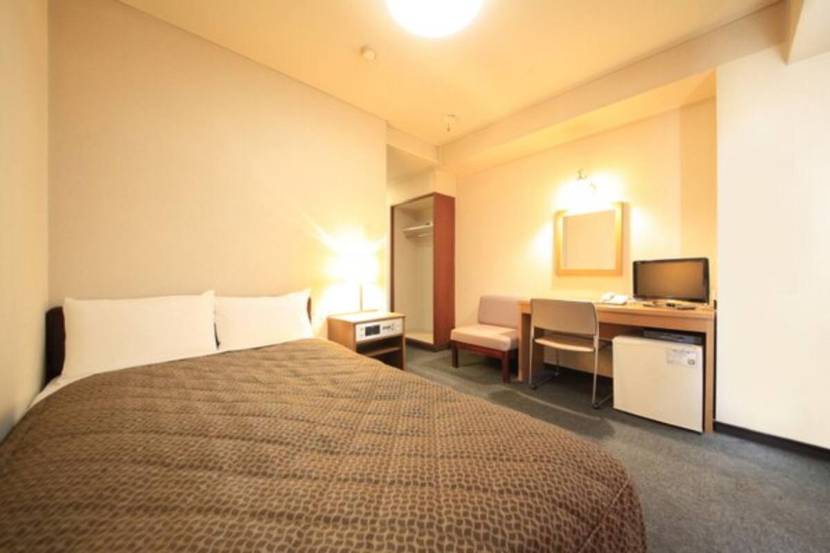Una habitación de hotel con una cama grande, un escritorio con computadora, una silla y un refrigerador pequeño.