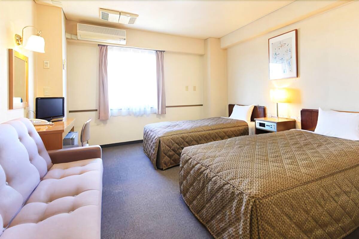 Habitación de hotel con dos camas, un escritorio, una silla, un televisor y una ventana con cortinas.