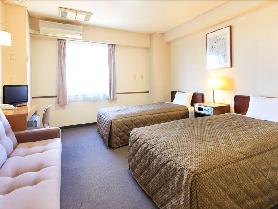Een hotelkamer met twee bedden, een bureau, een stoel, een televisie en een raam met gordijnen.